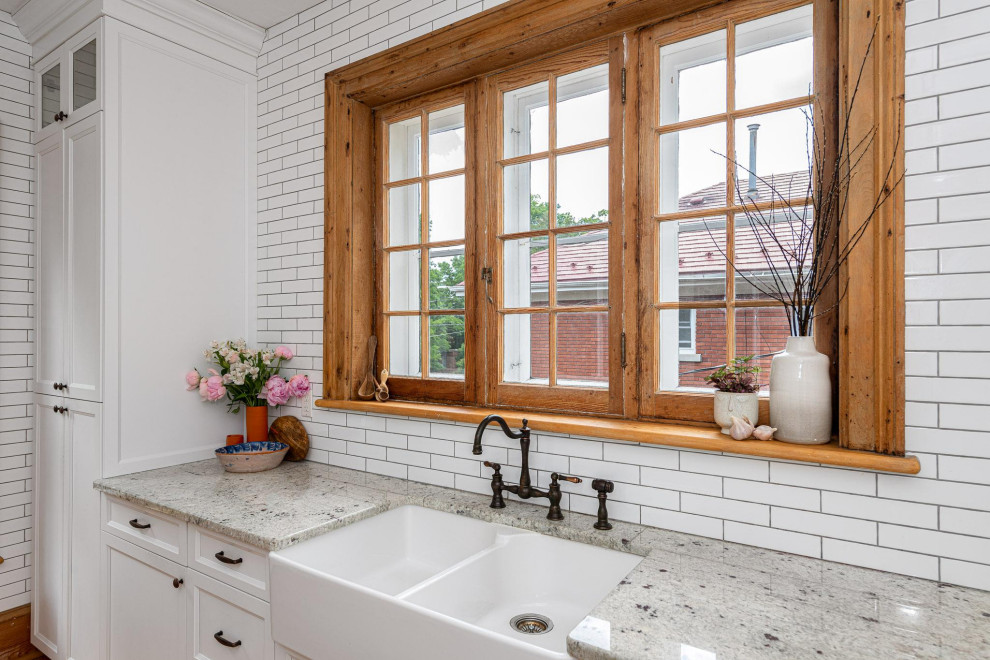 Enclosed kitchen - small transitional galley light wood floor and brown floor enclosed kitchen idea in Ottawa with a farmhouse sink, shaker cabinets, white cabinets, granite countertops, white backsplash, subway tile backsplash, stainless steel appliances, an island and gray countertops