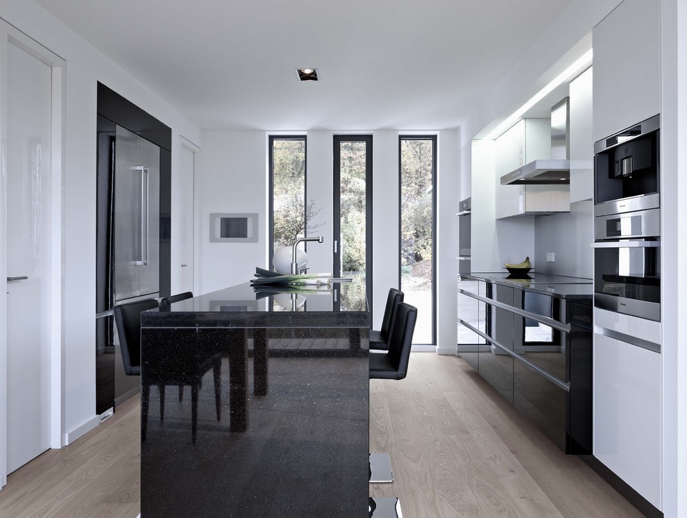 Inspiration for a mid-sized modern galley eat-in kitchen in Boston with an undermount sink, flat-panel cabinets, black cabinets, quartz benchtops, stainless steel appliances, light hardwood floors and with island.