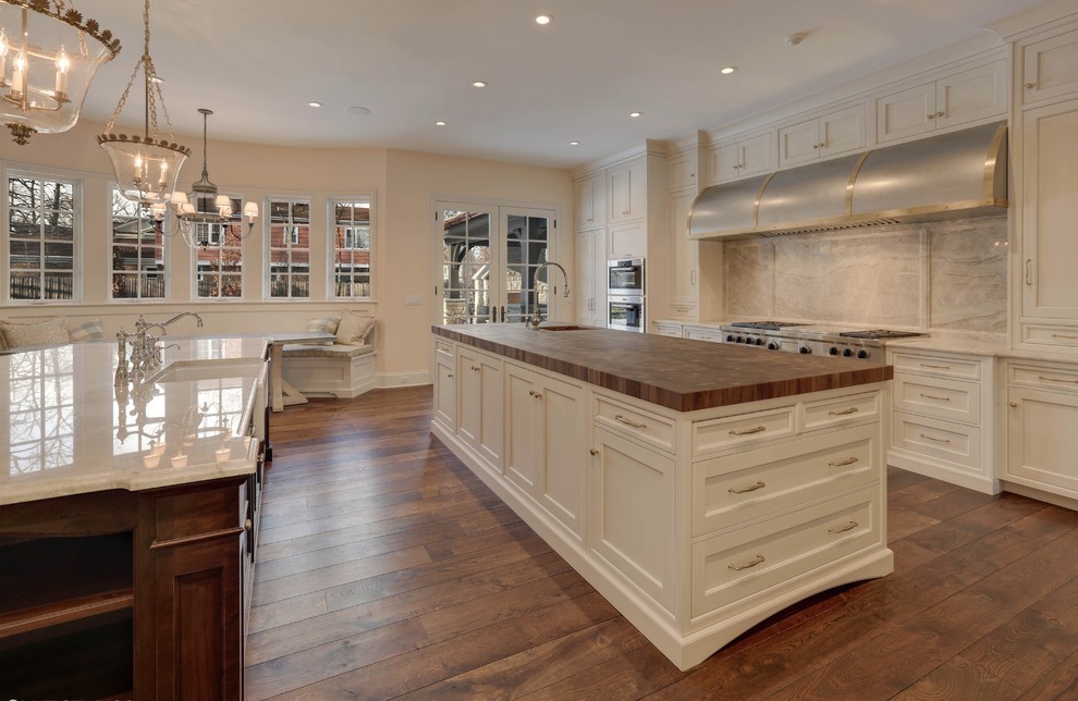 Design ideas for a large traditional kitchen in Chicago with a farmhouse sink, recessed-panel cabinets, white cabinets, wood benchtops, grey splashback, stone slab splashback, panelled appliances, medium hardwood floors and multiple islands.