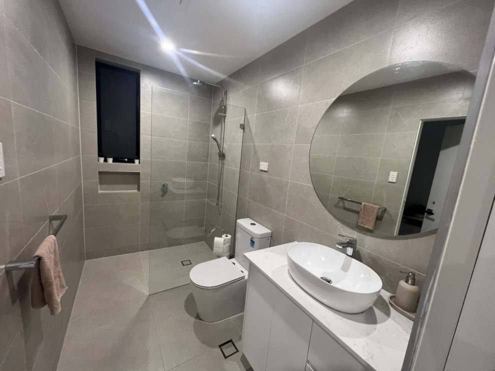 This is an example of a mid-sized modern master bathroom in Sydney with beaded inset cabinets, white cabinets, an open shower, a one-piece toilet, beige tile, ceramic tile, beige walls, ceramic floors, a vessel sink, quartzite benchtops, beige floor, white benchtops, a single vanity, a freestanding vanity and recessed.