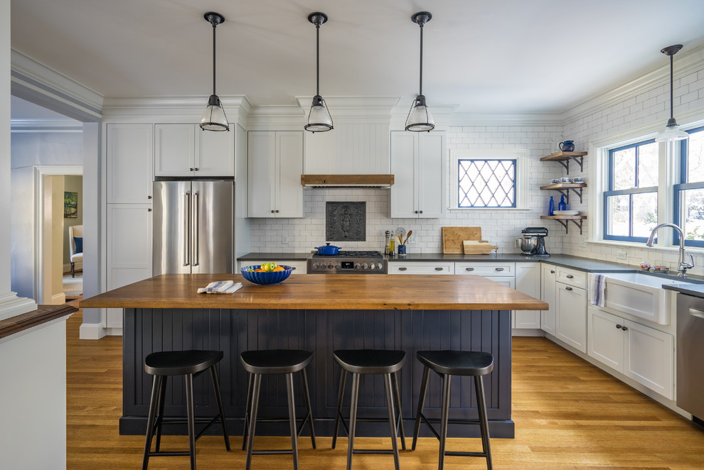 This is an example of a mid-sized country l-shaped eat-in kitchen in Boston with a farmhouse sink, shaker cabinets, white cabinets, quartz benchtops, white splashback, subway tile splashback, stainless steel appliances, medium hardwood floors and with island.