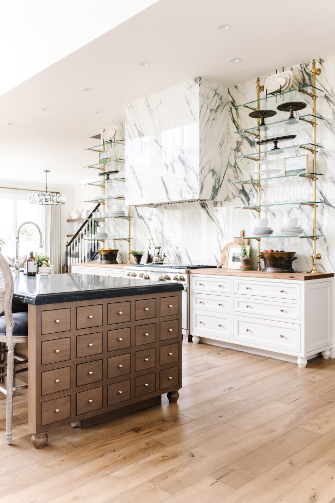 Example of a classic light wood floor kitchen design in Salt Lake City with a farmhouse sink, shaker cabinets, white cabinets, wood countertops, marble backsplash, stainless steel appliances, an island and black countertops