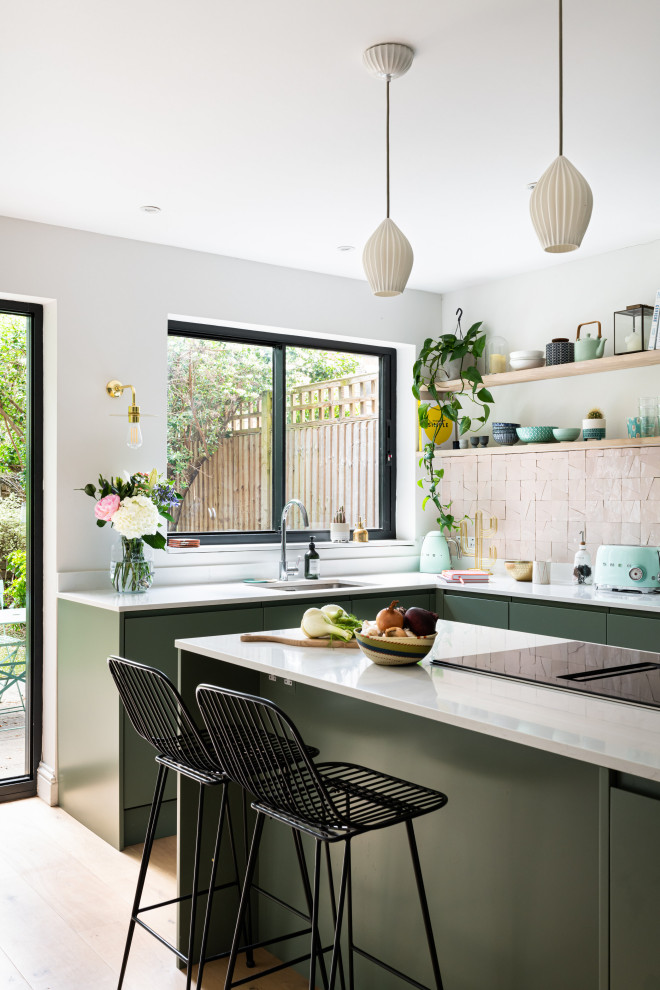 This is an example of a mid-sized eclectic u-shaped eat-in kitchen in London with an integrated sink, flat-panel cabinets, green cabinets, quartzite benchtops, cement tile splashback, panelled appliances, light hardwood floors, with island, beige floor and white benchtop.