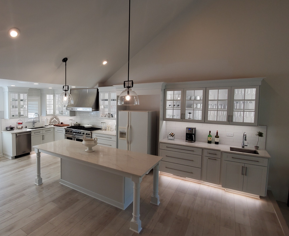 Example of a mid-sized transitional l-shaped laminate floor, beige floor and wallpaper ceiling eat-in kitchen design in Chicago with an undermount sink, glass-front cabinets, white cabinets, quartzite countertops, white backsplash, ceramic backsplash, stainless steel appliances, an island and white countertops