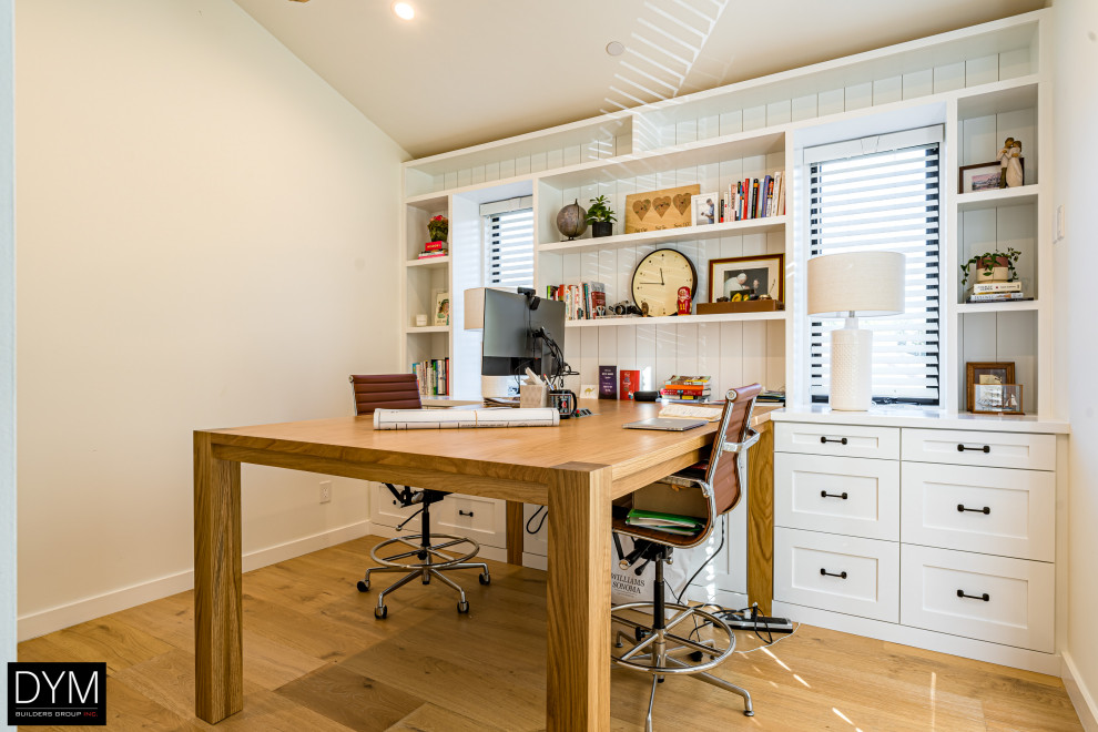 Modelo de despacho actual de tamaño medio con biblioteca, paredes blancas, suelo de madera clara, escritorio empotrado, suelo marrón, papel pintado y papel pintado