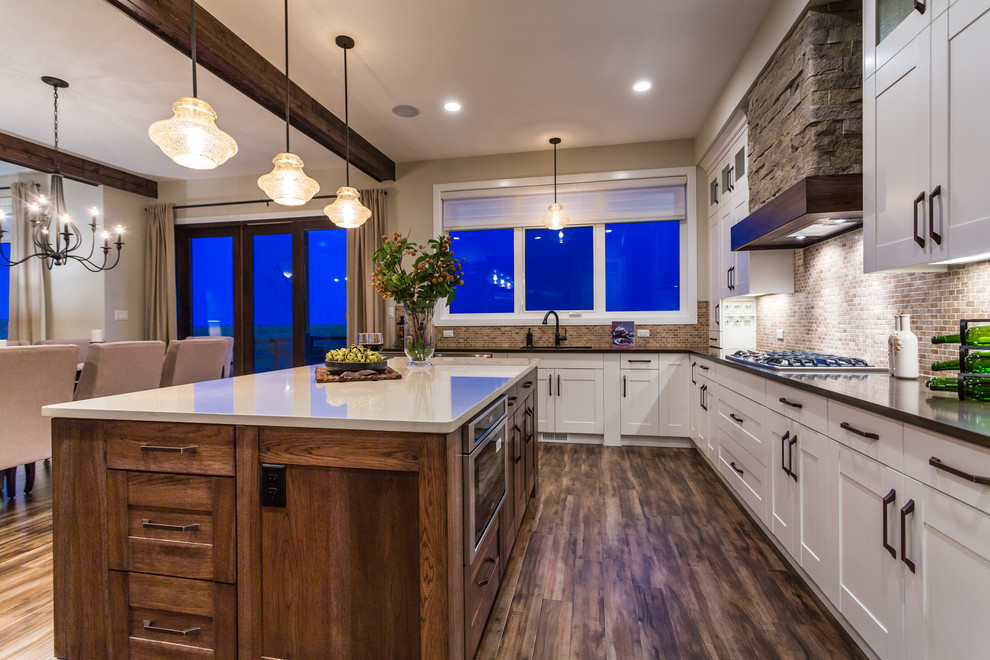Photo of a large transitional u-shaped eat-in kitchen in Calgary with an undermount sink, shaker cabinets, white cabinets, quartz benchtops, brown splashback, ceramic splashback, stainless steel appliances, dark hardwood floors and with island.