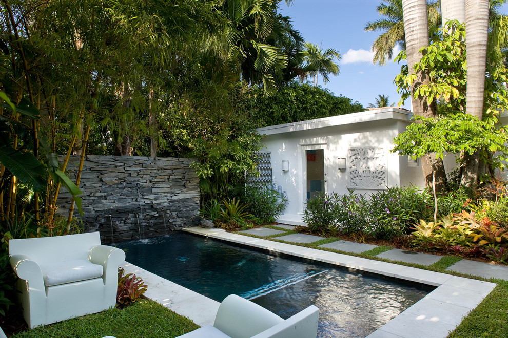 Photo of a small tropical backyard rectangular lap pool in Miami with concrete pavers and a water feature.