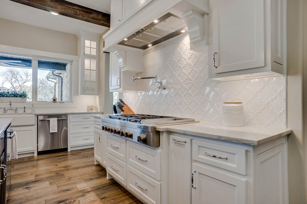 Inspiration for a large traditional u-shaped open plan kitchen in Dallas with a farmhouse sink, shaker cabinets, brown cabinets, quartzite benchtops, white splashback, ceramic splashback, stainless steel appliances, medium hardwood floors, with island, brown floor and white benchtop.