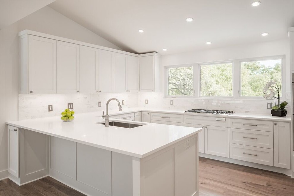 Transitional u-shaped medium tone wood floor enclosed kitchen photo in Austin with shaker cabinets, white cabinets, quartz countertops, white backsplash, stone tile backsplash, stainless steel appliances and a peninsula