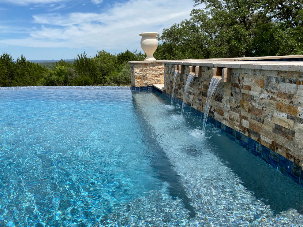 Expansive modern backyard custom-shaped infinity pool in Austin with with privacy feature and decking.