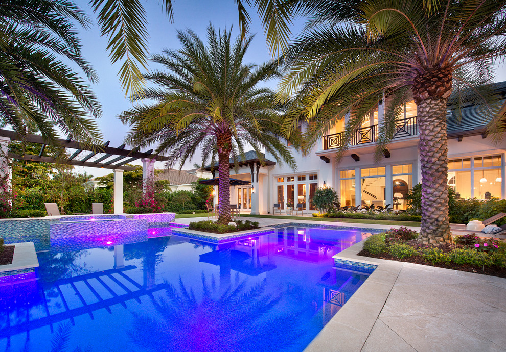 Large tropical backyard custom-shaped infinity pool in Miami with a hot tub and natural stone pavers.