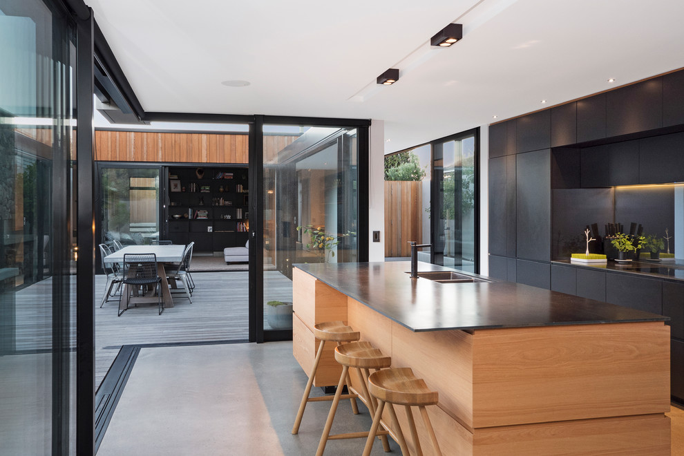 Inspiration for a contemporary galley eat-in kitchen in Christchurch with a double-bowl sink, flat-panel cabinets, black cabinets, mirror splashback, concrete floors, with island, grey floor and black benchtop.