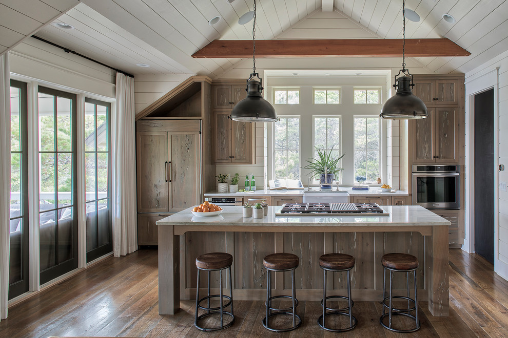 This is an example of a beach style galley kitchen in Other with a farmhouse sink, shaker cabinets, medium wood cabinets, white splashback, panelled appliances, medium hardwood floors, with island, brown floor and white benchtop.
