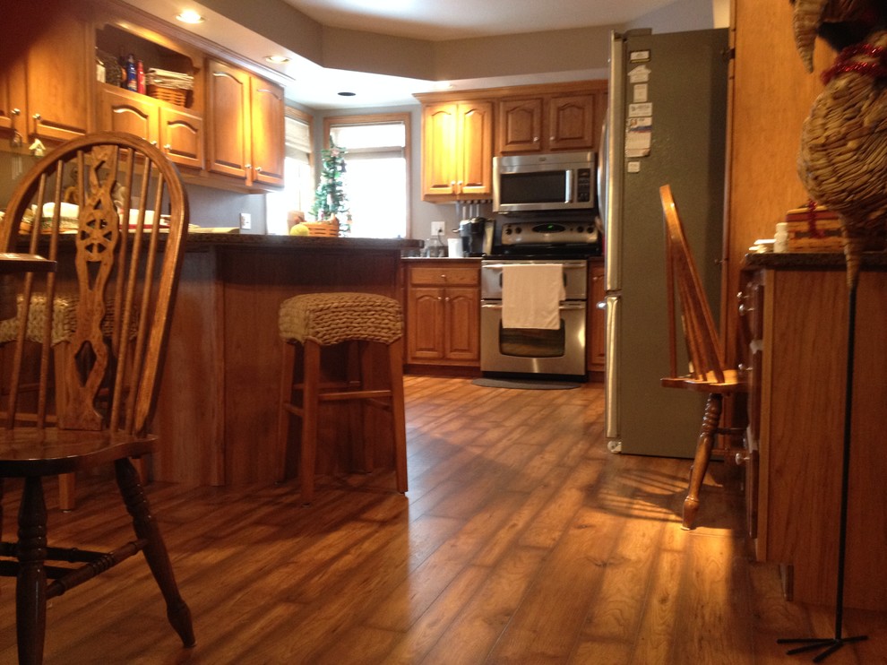 This is an example of a mid-sized traditional u-shaped eat-in kitchen in Cedar Rapids with raised-panel cabinets, medium wood cabinets, granite benchtops, beige splashback, stainless steel appliances, dark hardwood floors and a peninsula.