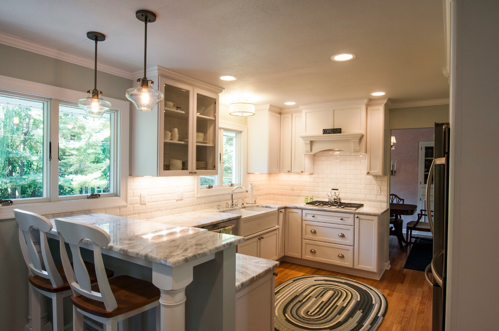 Small transitional u-shaped medium tone wood floor enclosed kitchen photo in Milwaukee with a farmhouse sink, shaker cabinets, white cabinets, granite countertops, white backsplash, subway tile backsplash, stainless steel appliances and a peninsula