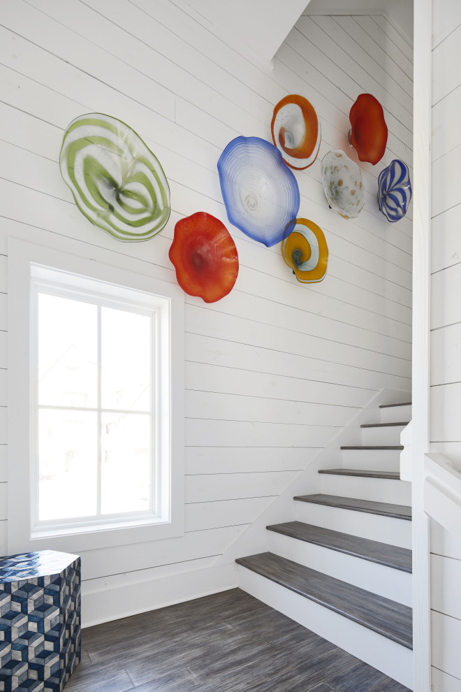 This is an example of a mid-sized beach style wood u-shaped staircase in Other with planked wall panelling and painted wood risers.