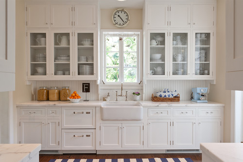 Bright kitchen with white shaker RTA cabinets, glass-front uppers, a farmhouse sink, and marble-look countertops.