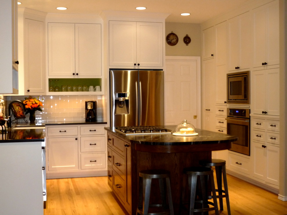 This is an example of a transitional u-shaped eat-in kitchen in Portland with white cabinets, granite benchtops, white splashback, glass tile splashback, stainless steel appliances, medium hardwood floors, with island, a farmhouse sink and shaker cabinets.