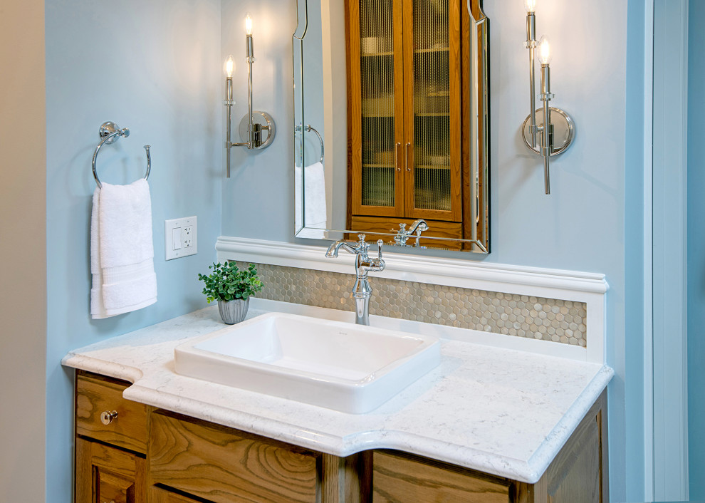 Photo of a mid-sized transitional master bathroom in Atlanta with raised-panel cabinets, medium wood cabinets, a freestanding tub, a corner shower, a two-piece toilet, metal tile, blue walls, limestone floors, a vessel sink, engineered quartz benchtops, grey floor, a hinged shower door, white benchtops, an enclosed toilet, a single vanity and timber.