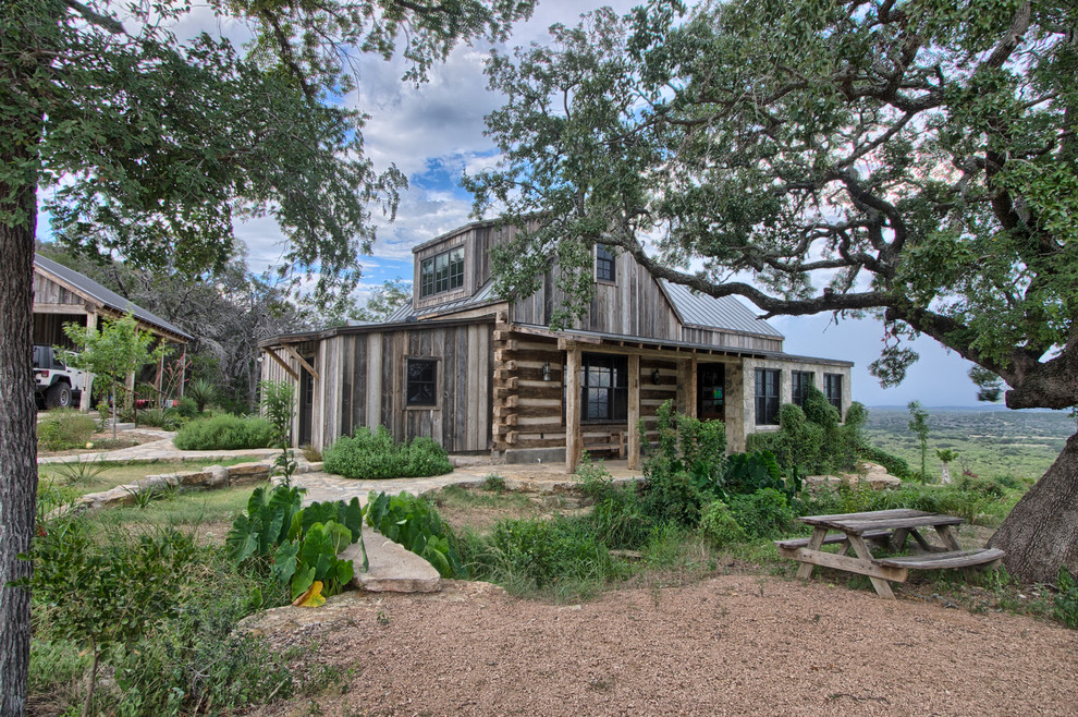 Photo of a mid-sized country two-storey grey house exterior in Austin with stone veneer, a gable roof and a metal roof.