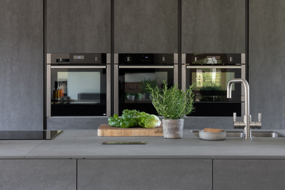 Aménagement d'une grande cuisine américaine encastrable et grise et noire moderne avec un évier 2 bacs, un placard à porte plane, des portes de placard grises, un sol en carrelage de céramique, îlot et un sol noir.