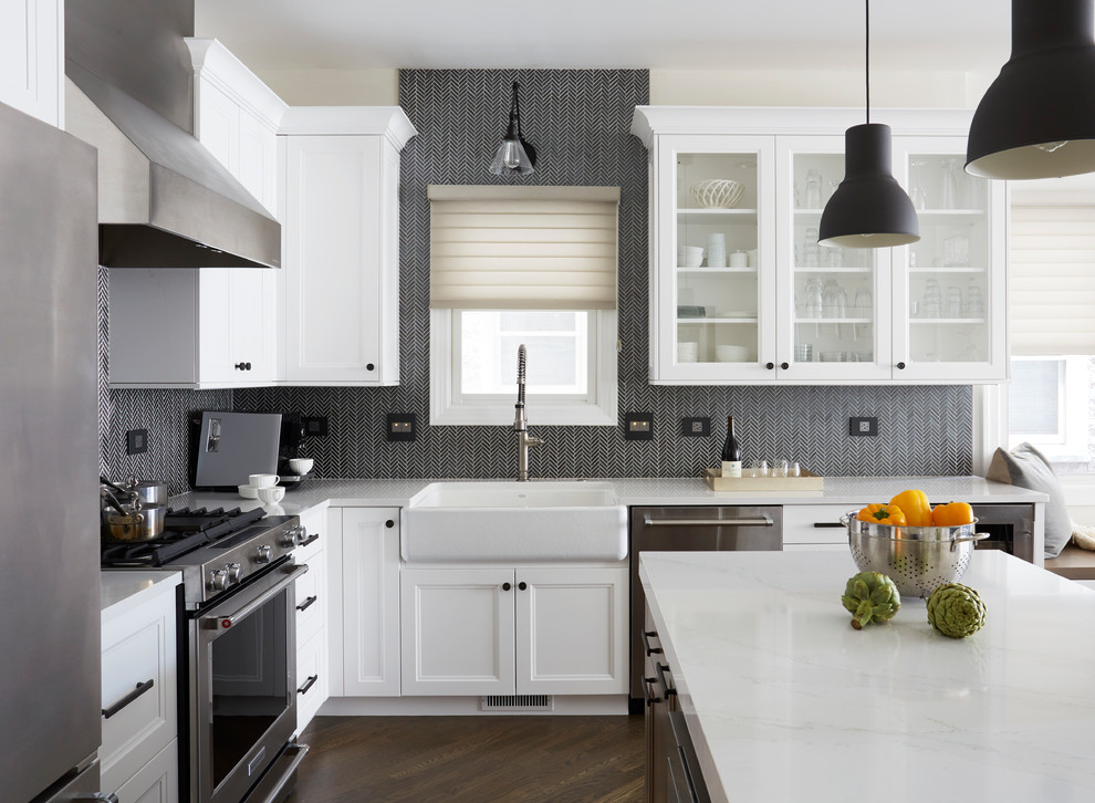 Transitional u-shaped eat-in kitchen in Chicago with a farmhouse sink, recessed-panel cabinets, white cabinets, black splashback, stainless steel appliances, dark hardwood floors, with island, white benchtop and brown floor.