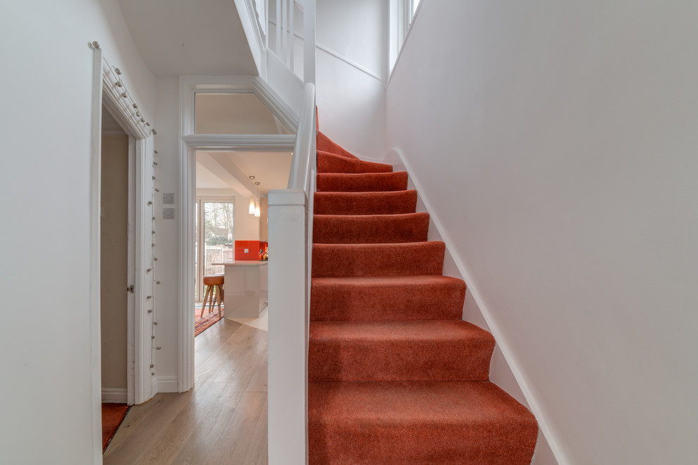 Photo of a mid-sized modern carpeted straight staircase in London with carpet risers and wood railing.