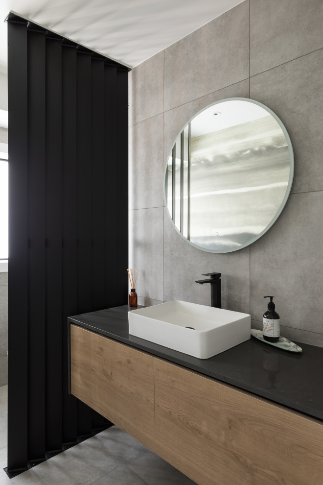 Mid-sized contemporary bathroom in Auckland with medium wood cabinets, cement tile, engineered quartz benchtops, black benchtops, a single vanity, a floating vanity and gray tile.