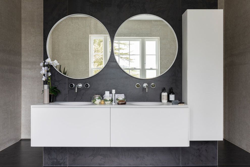 Large contemporary bathroom in London with flat-panel cabinets, white cabinets, a freestanding tub, an open shower, a one-piece toilet, black and white tile, black walls, an undermount sink, solid surface benchtops, black floor and cement tiles.