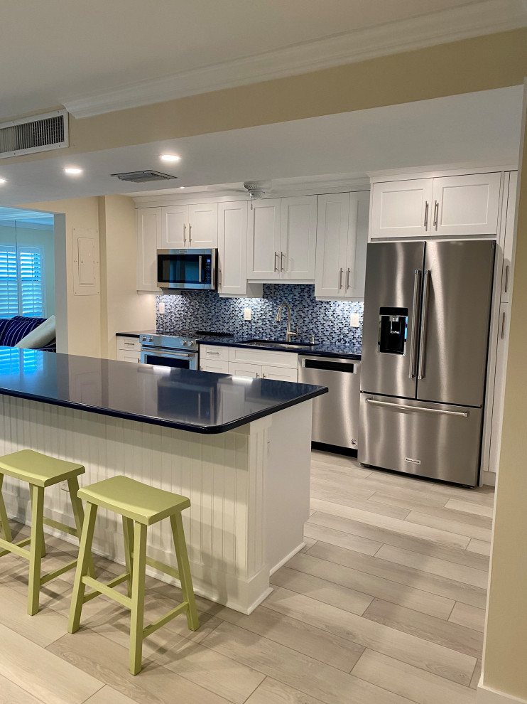 Modern inredning av ett mellanstort blå blått kök, med skåp i shakerstil, vita skåp, en köksö, bänkskiva i kvarts, en undermonterad diskho, blått stänkskydd, stänkskydd i stickkakel, rostfria vitvaror, vinylgolv och brunt golv