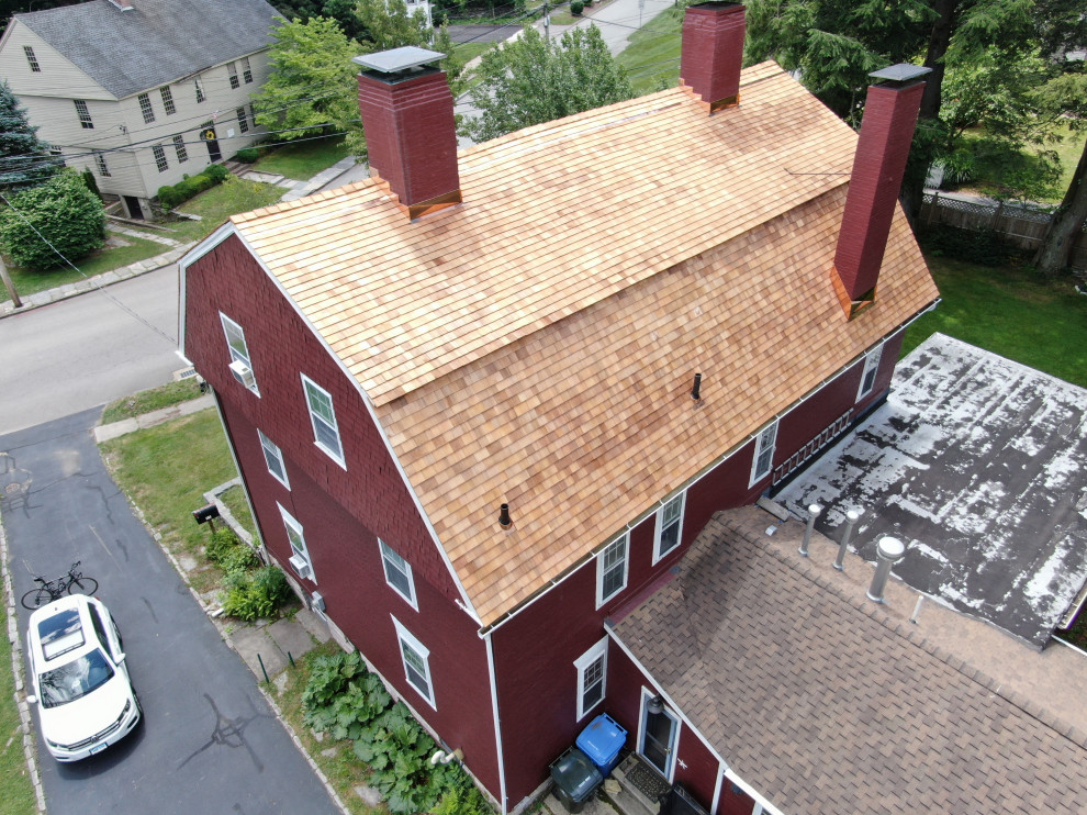 Immagine della villa grande rossa classica a tre piani con rivestimento in mattone verniciato, tetto a mansarda, copertura a scandole e tetto rosso