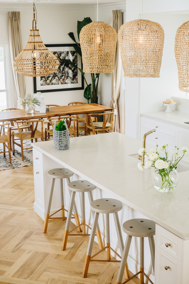 This is an example of a small shabby-chic style galley open plan kitchen in Brisbane with a double-bowl sink, recessed-panel cabinets, white cabinets, quartz benchtops, white splashback, black appliances, medium hardwood floors, with island, brown floor and beige benchtop.