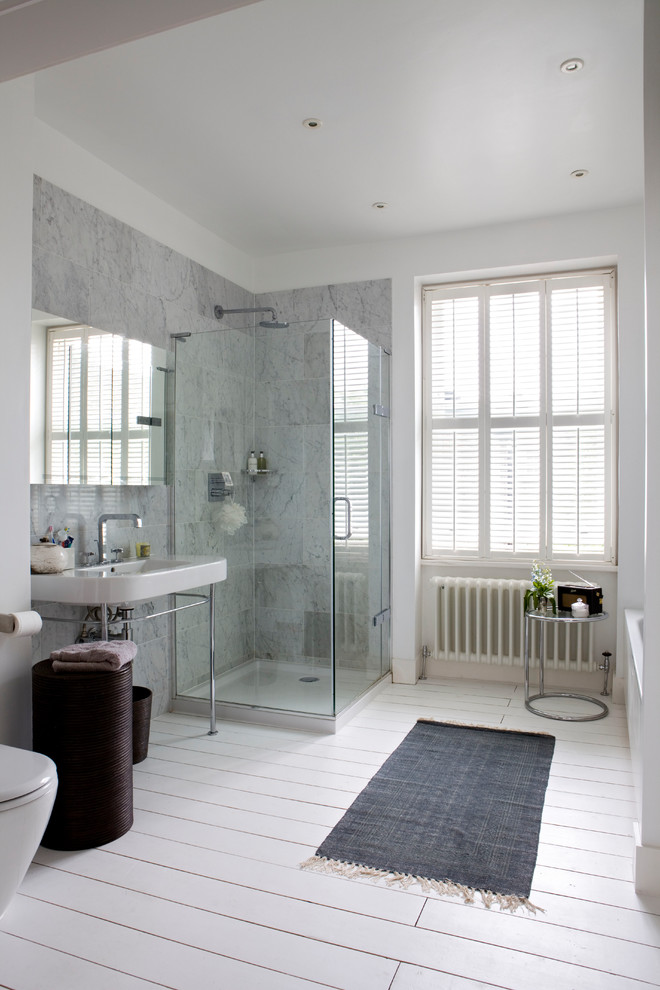 This is an example of a transitional bathroom in London with a drop-in tub, a corner shower, gray tile, white walls, painted wood floors, a wall-mount sink, white floor and a hinged shower door.