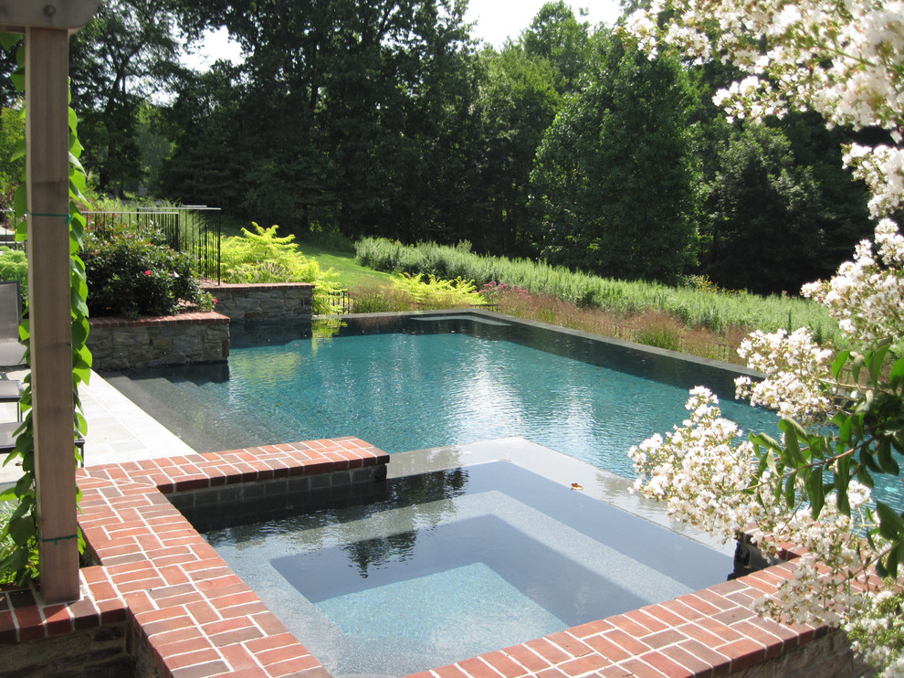 Photo of a large contemporary backyard rectangular infinity pool in Philadelphia with a hot tub and brick pavers.