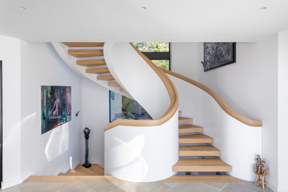 This is an example of a contemporary wood curved staircase in Devon with open risers.