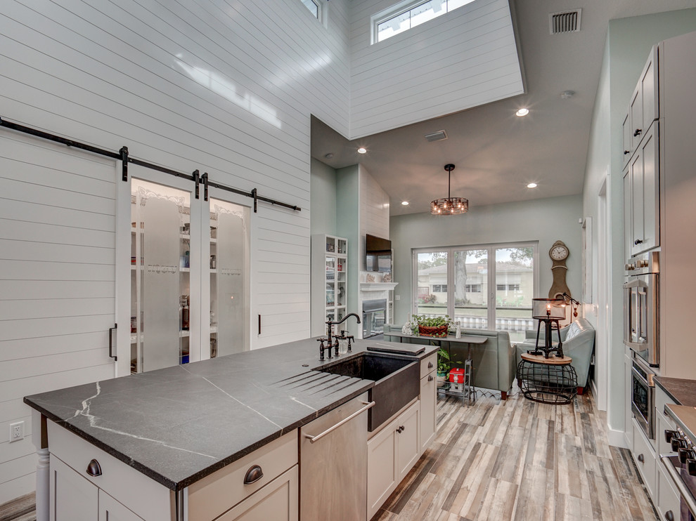 Inspiration for a mid-sized beach style galley eat-in kitchen in Tampa with an integrated sink, shaker cabinets, grey cabinets, quartz benchtops, white splashback, ceramic splashback, stainless steel appliances, ceramic floors, with island, grey floor and grey benchtop.