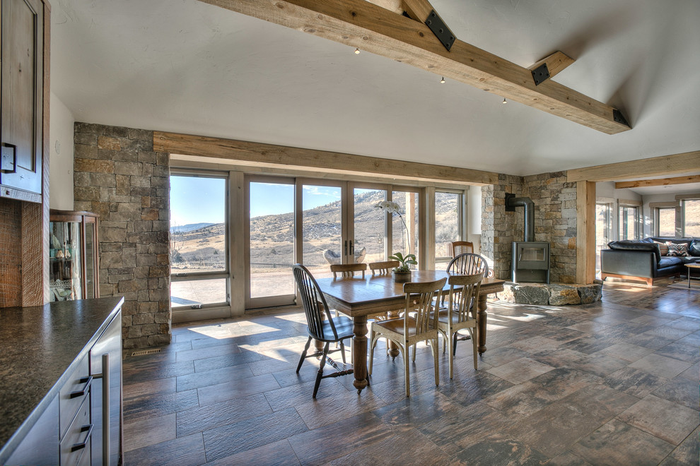 Kitchen/dining room combo - rustic ceramic tile kitchen/dining room combo idea in Denver with gray walls, a wood stove and a stone fireplace