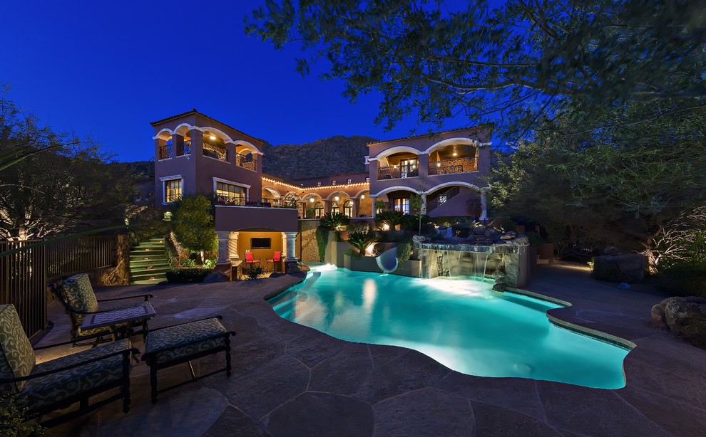 Expansive mediterranean backyard custom-shaped natural pool in Phoenix with a water feature and natural stone pavers.