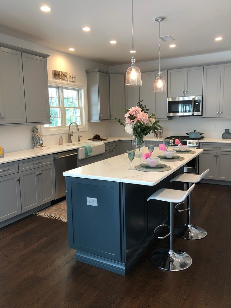 Mid-sized transitional l-shaped open plan kitchen in New York with a farmhouse sink, shaker cabinets, grey cabinets, quartzite benchtops, stainless steel appliances, medium hardwood floors, with island, brown floor and yellow benchtop.