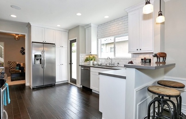 Mid-sized transitional l-shaped separate kitchen in Los Angeles with an undermount sink, recessed-panel cabinets, white cabinets, solid surface benchtops, white splashback, subway tile splashback, stainless steel appliances and dark hardwood floors.