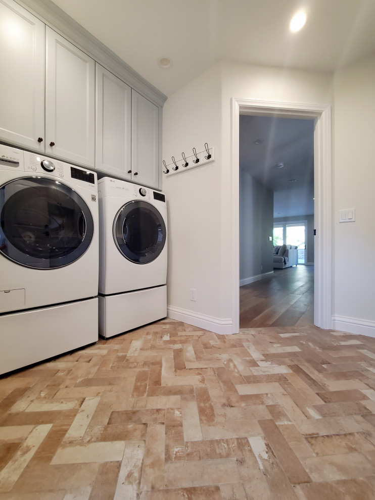 Inspiration for a mid-sized galley dedicated laundry room in Orange County with a farmhouse sink, raised-panel cabinets, blue cabinets, quartz benchtops, white splashback, engineered quartz splashback, beige walls, brick floors, a side-by-side washer and dryer and white benchtop.