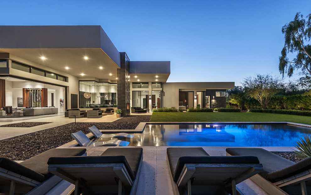 This is an example of an expansive contemporary backyard custom-shaped infinity pool in Phoenix with natural stone pavers.