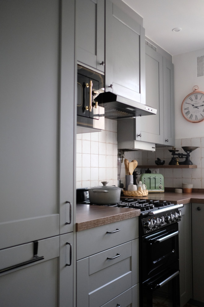 Photo of a small traditional u-shaped separate kitchen in Paris with a farmhouse sink, grey cabinets, wood benchtops, ceramic splashback, ceramic floors, orange floor, brown benchtop, beaded inset cabinets, white splashback, black appliances and no island.