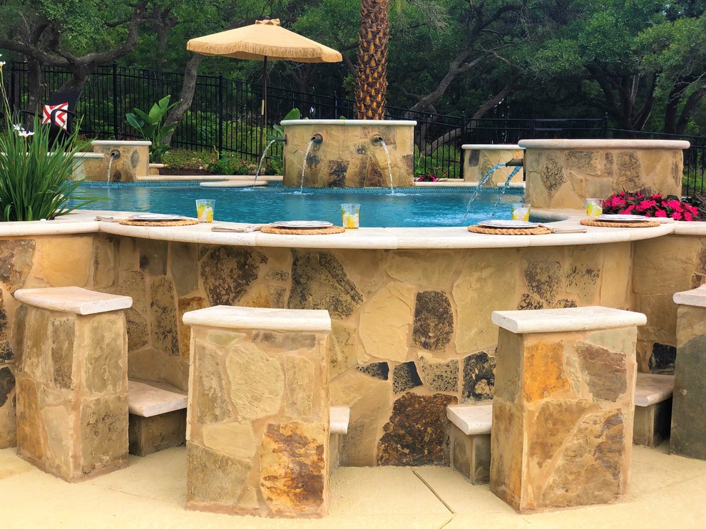 This is an example of a large tropical backyard kidney-shaped natural pool in Austin with a water feature and decking.