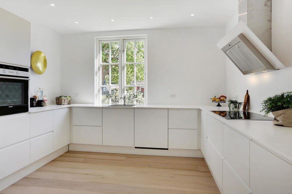 Photo of a scandinavian u-shaped kitchen in Copenhagen with flat-panel cabinets, white cabinets, stainless steel appliances, light hardwood floors, no island and beige floor.