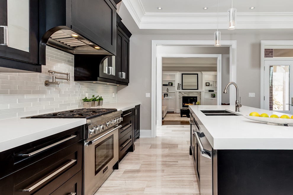 Photo of a transitional l-shaped kitchen in Toronto with an undermount sink, shaker cabinets, dark wood cabinets, solid surface benchtops, white splashback, glass tile splashback, stainless steel appliances and marble floors.