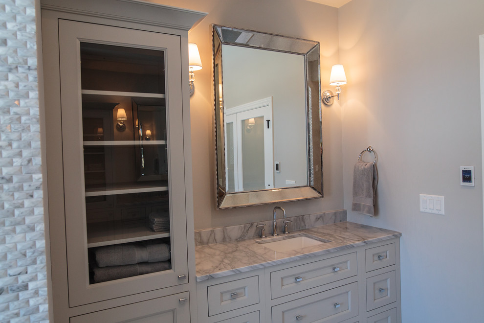 This is an example of a large transitional master wet room bathroom in Chicago with shaker cabinets, grey cabinets, a freestanding tub, a two-piece toilet, gray tile, marble, brown walls, an undermount sink, marble benchtops and marble floors.