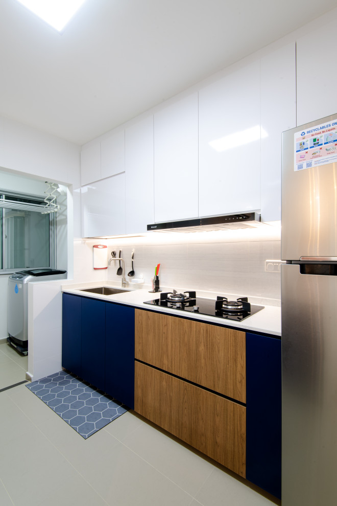 This is an example of a mid-sized contemporary single-wall kitchen in Singapore with an undermount sink, flat-panel cabinets, blue cabinets, white splashback, no island, grey floor and white benchtop.