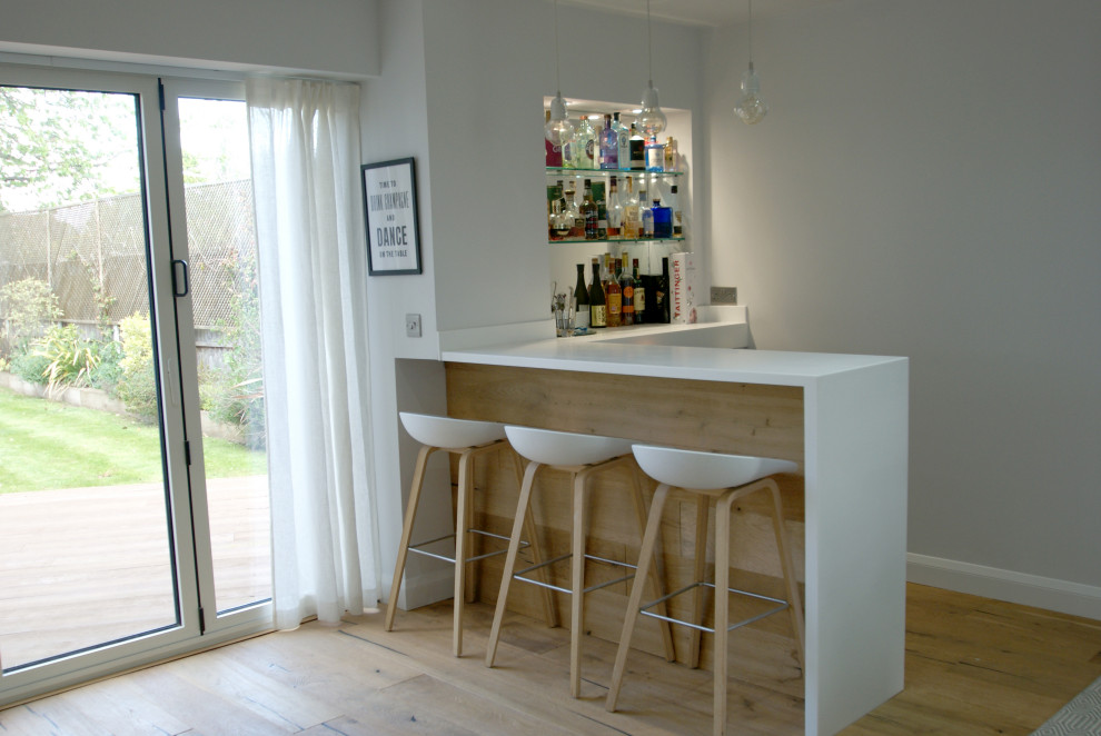 Foto di un grande bancone bar nordico con top in superficie solida, paraspruzzi bianco, pavimento in legno massello medio e top bianco