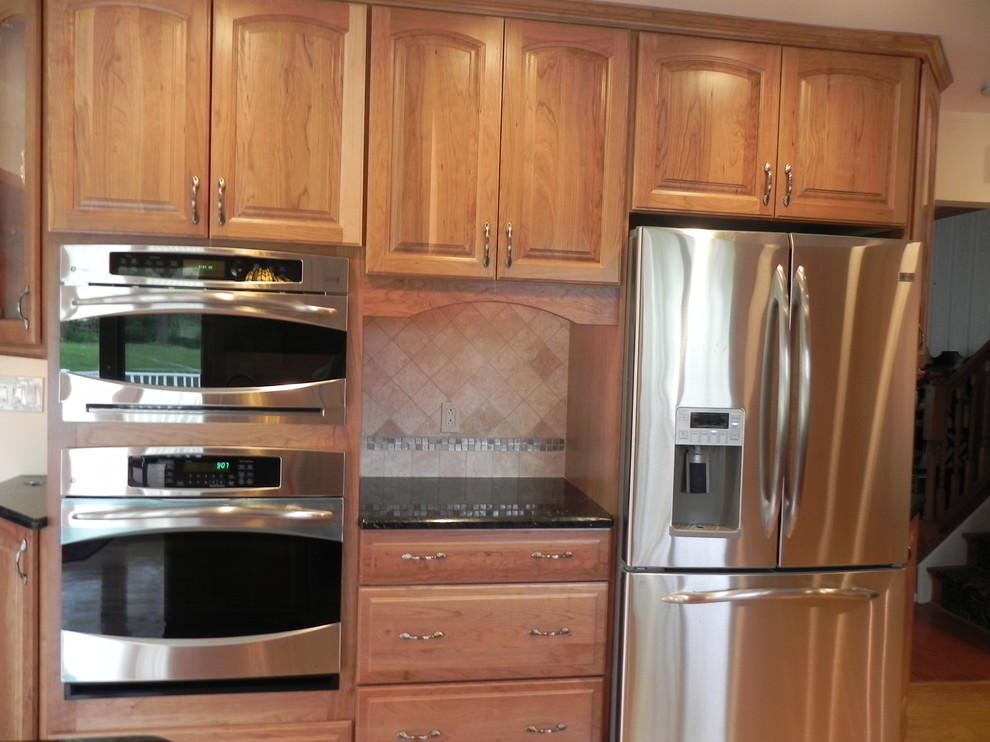 Inspiration for a mid-sized timeless u-shaped medium tone wood floor eat-in kitchen remodel in Philadelphia with an undermount sink, raised-panel cabinets, medium tone wood cabinets, granite countertops, beige backsplash, stone tile backsplash, stainless steel appliances and a peninsula